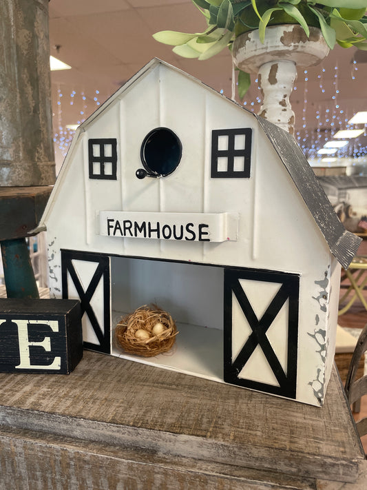Farmhouse-style birdhouse with a decorative egg on a wooden surface