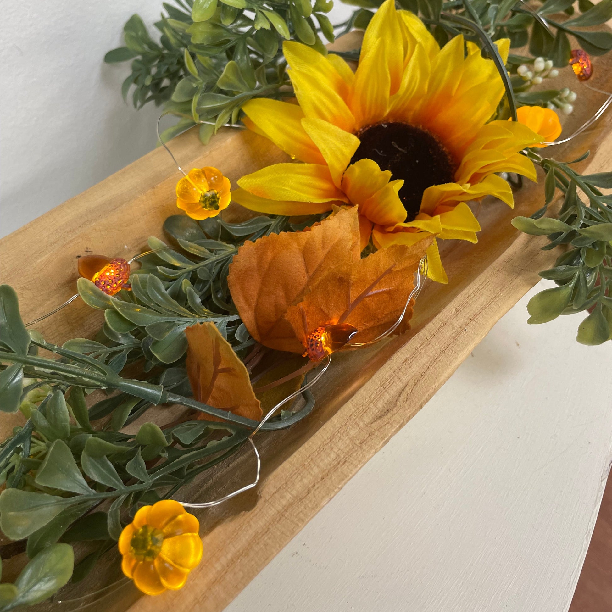 Decorative garland with sunflowers and greenery on a wooden board.