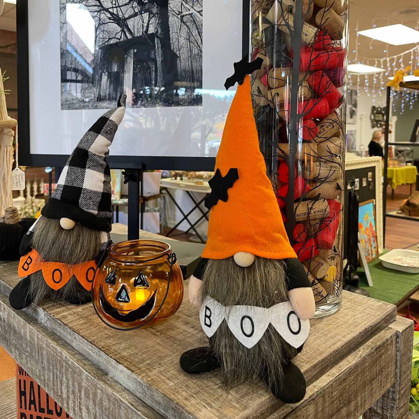 Halloween-themed decoration with a raccoon figurine holding a pumpkin and 'BOO' sign, in front of a black and white photo.