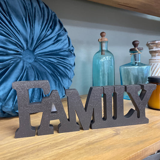 Decorative metal word sculpture spelling 'FAMILY' on a wooden surface with bottles in the background.