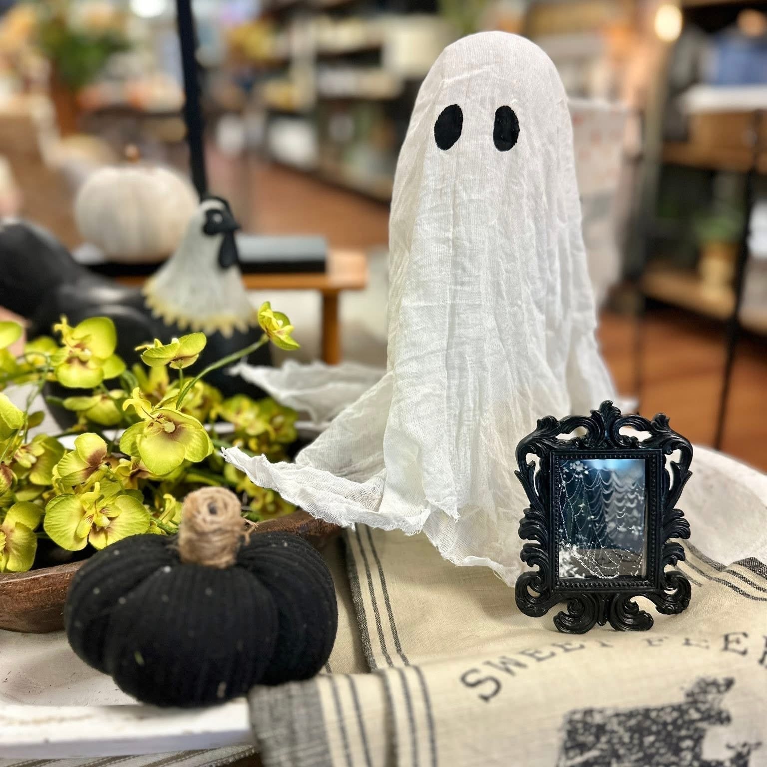 Small ghost decoration on a table with pumpkins and a framed picture in a store setting